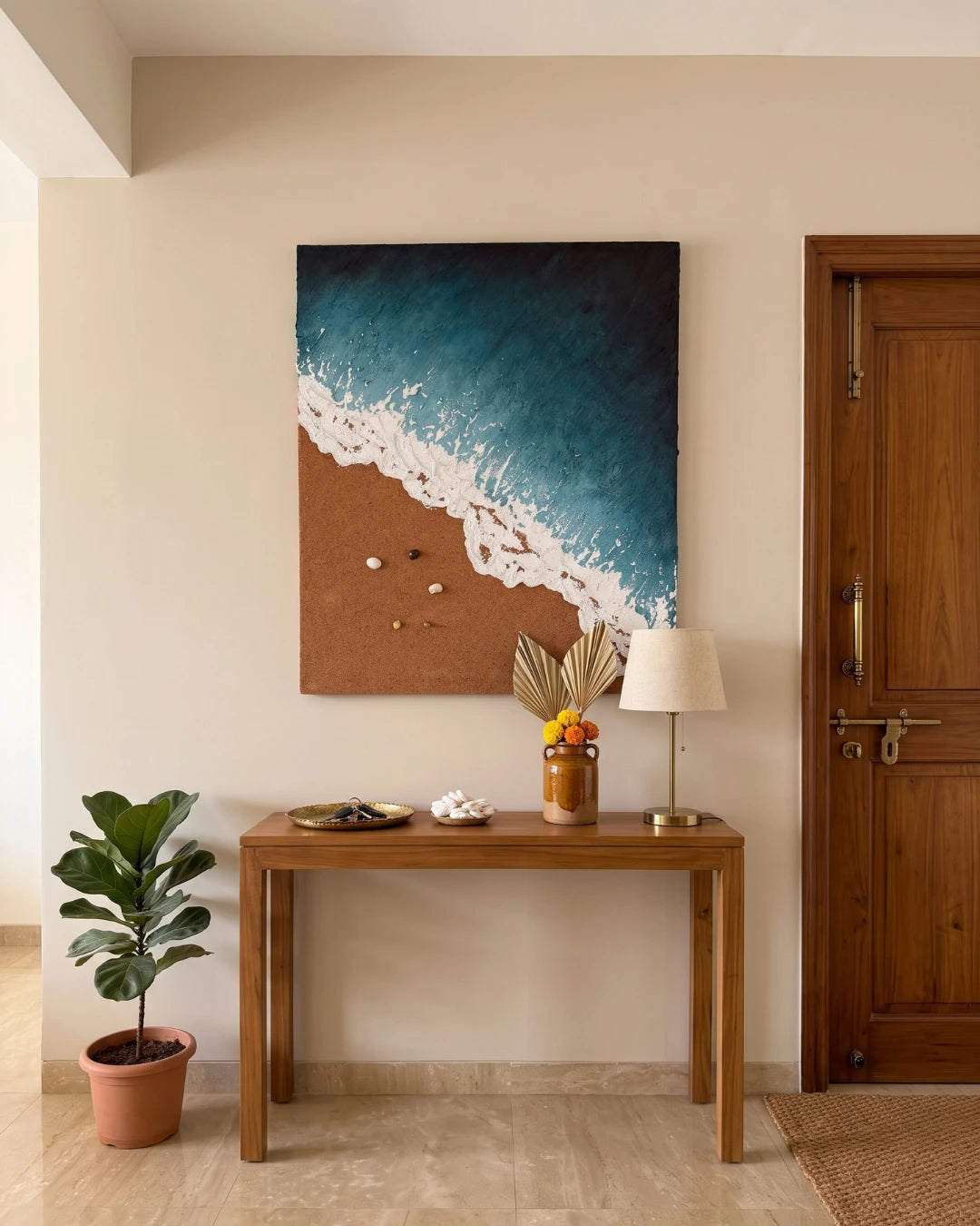 A vertical canvas wall art print depicting a beach scene with deep blue ocean waves crashing onto a brown sandy shore, displayed in a styled interior above a wooden console table.