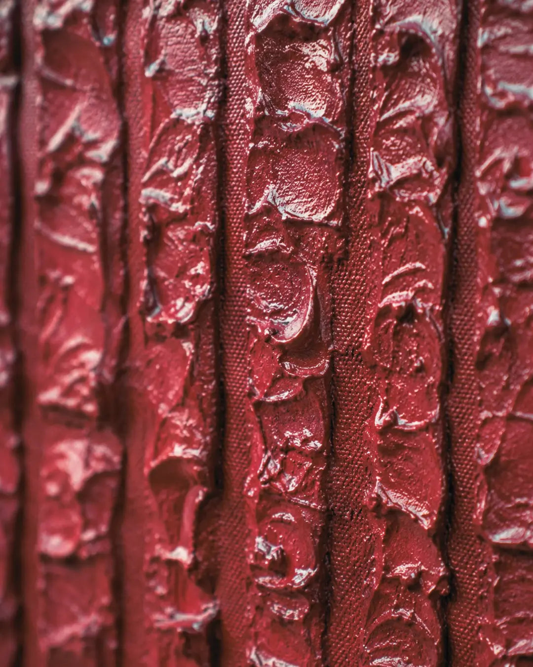 A close-up of a textured red fabric or wallpaper with vertical ridges and a glossy, embossed finish.