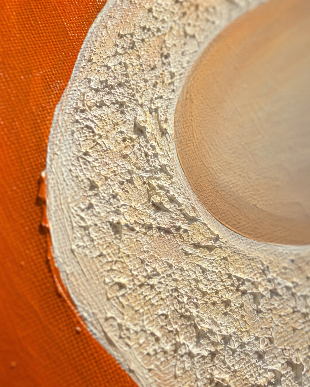 A close-up of a textured, off-white woven or fibrous material with a circular opening, positioned over a vibrant orange background.