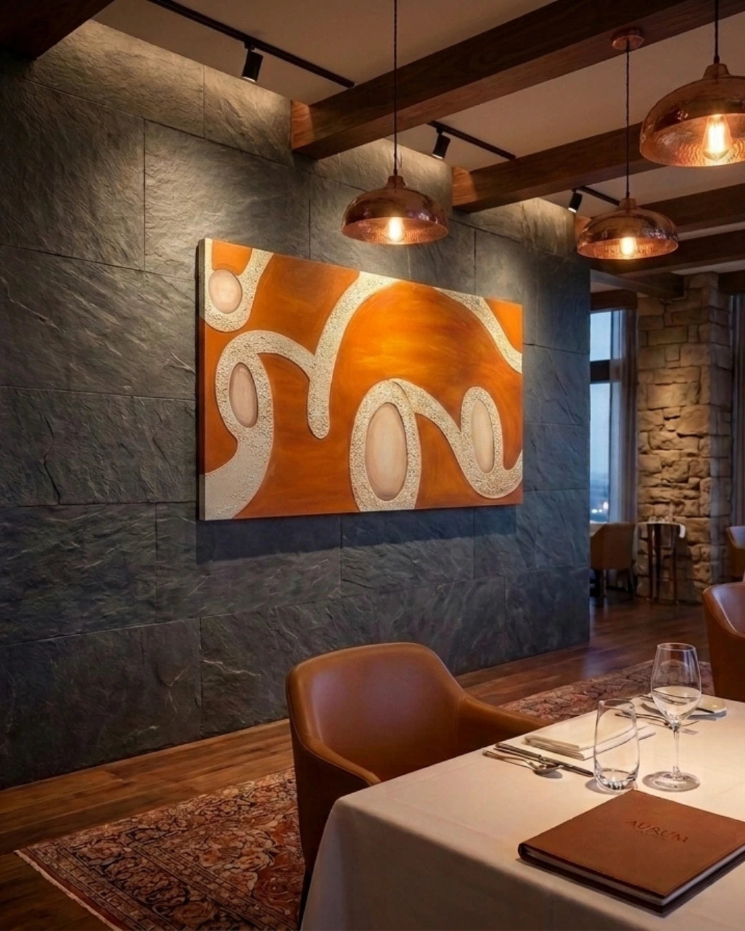An abstract canvas painting with orange and white wavy patterns displayed on a dark slate wall in a restaurant setting with wooden ceiling beams, pendant lights, and dining tables.