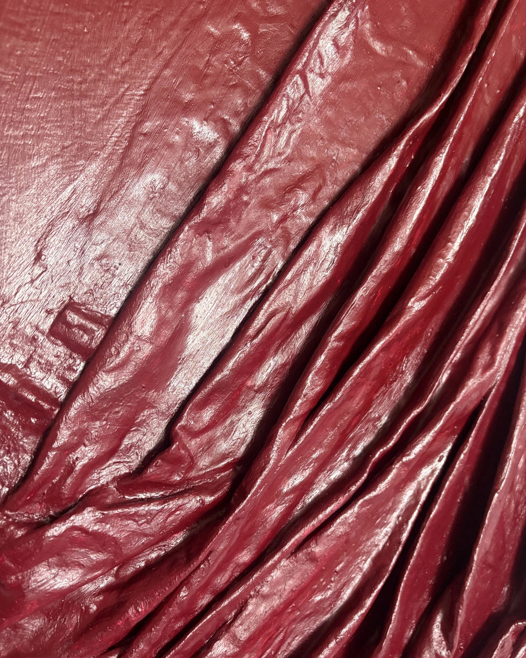 A close-up of draped, glossy burgundy red fabric with visible folds and texture.