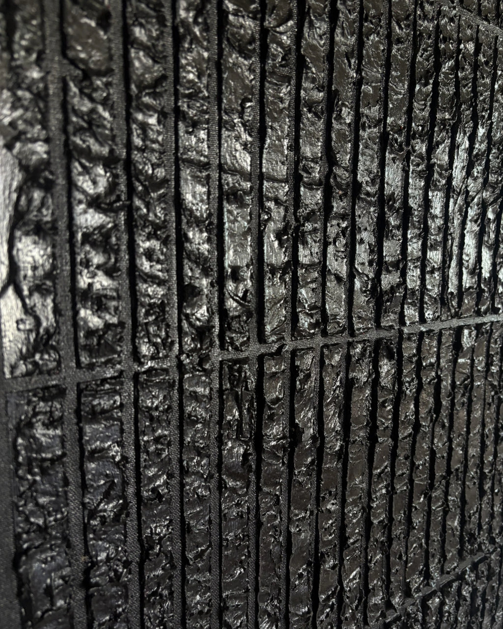 A close-up of a dark textured material with a vertical slatted or ribbed pattern, shown in high detail.