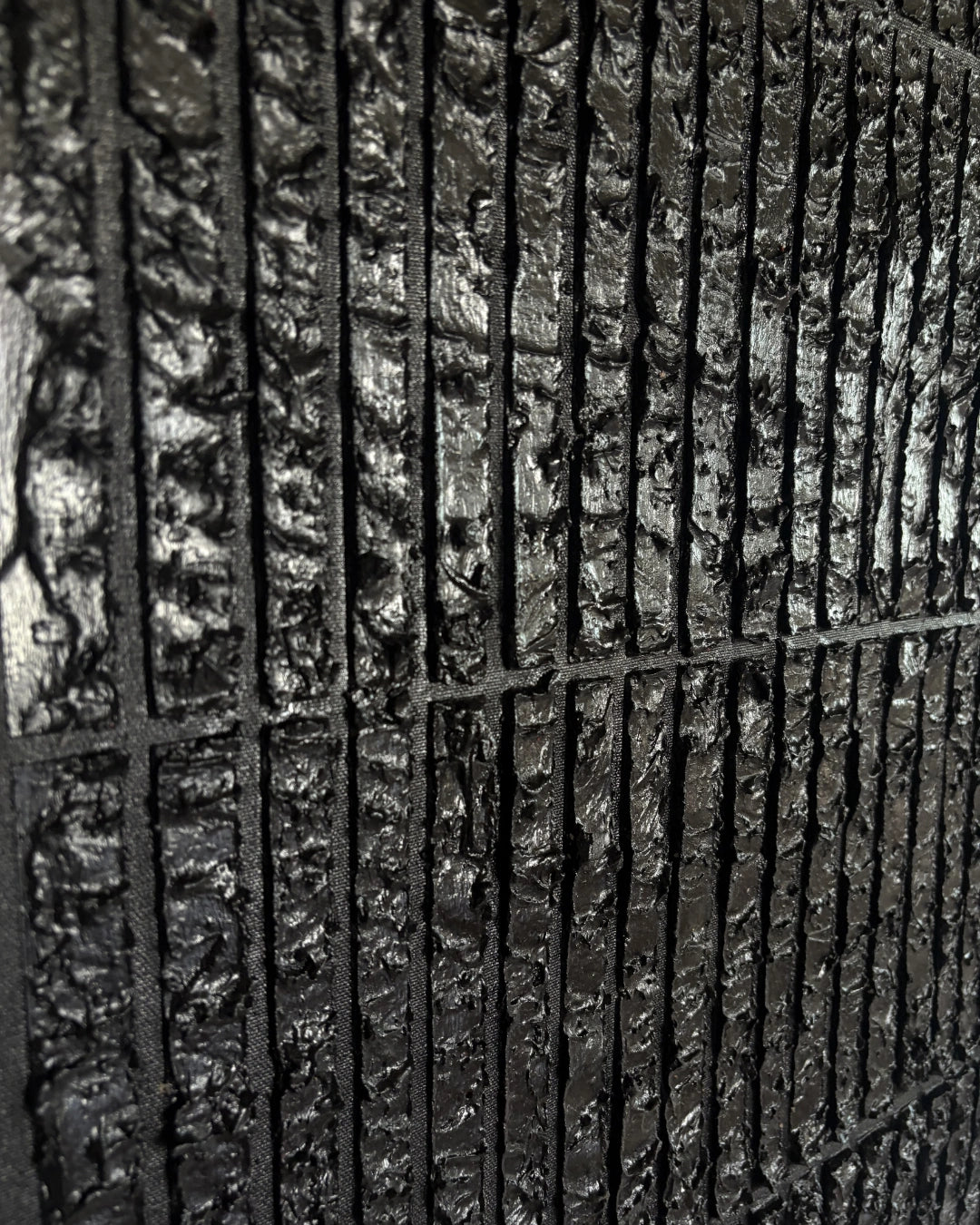 A close-up of a dark textured material with a vertical slatted or ribbed pattern, shown in high detail.