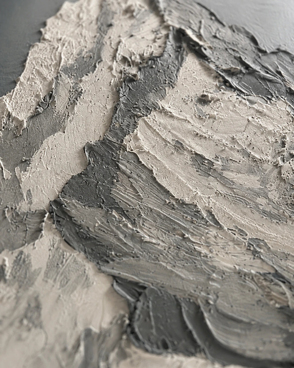 Close-up of a thick, textured gray and off-white paint or plaster surface with layered brushstrokes and ridges.