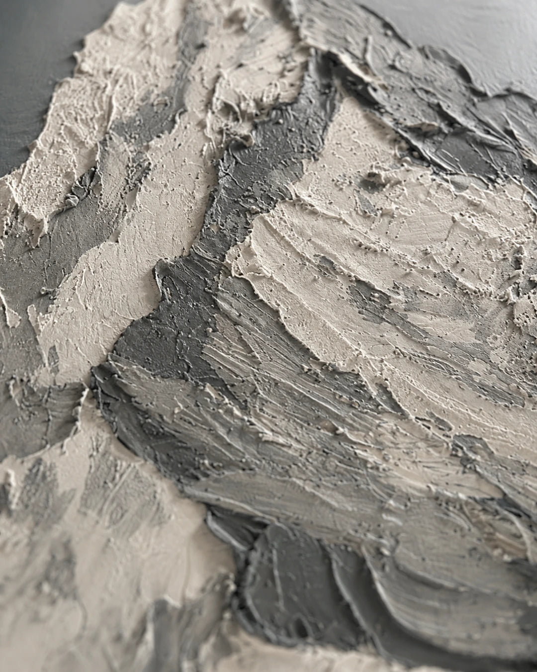 Close-up of a thick, textured gray and off-white paint or plaster surface with layered brushstrokes and ridges.