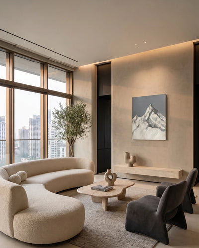 A modern living room featuring a curved cream bouclé sofa, dark gray accent chairs, a light wood coffee table, and a large canvas print of a snow-capped mountain on a beige textured wall.