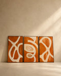 Handmade rust orange abstract triptych featuring three textured canvas panels with flowing ivory sculptural forms, creating a bold modern statement wall art arrangement.