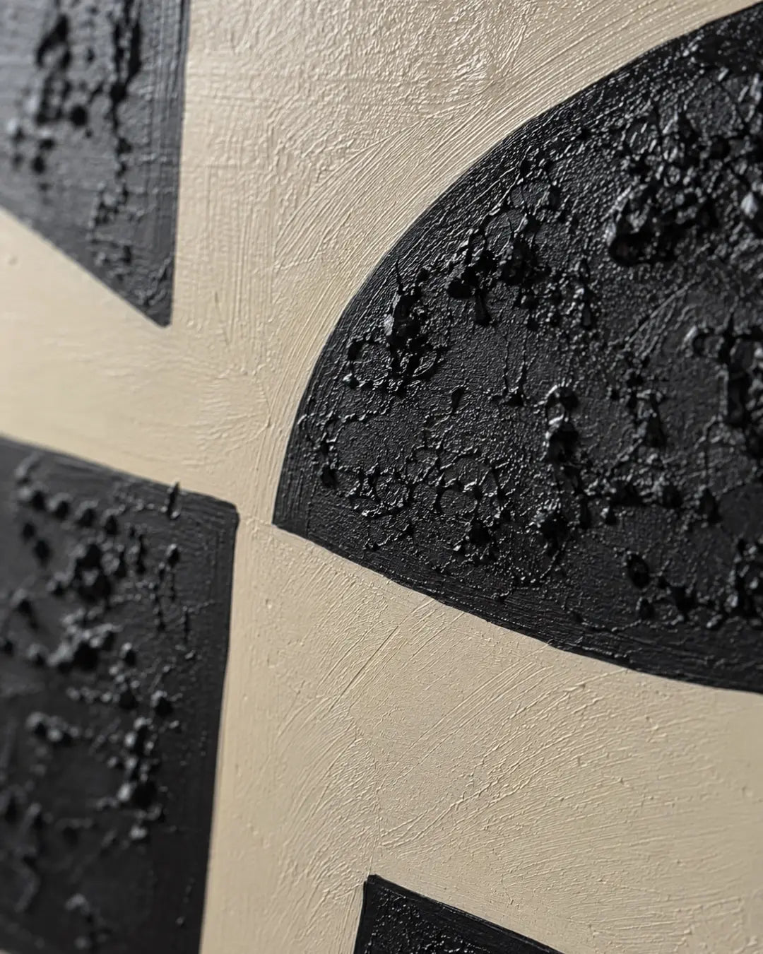 Close-up of a textured abstract wall art piece featuring black organic geometric shapes on a warm beige background.