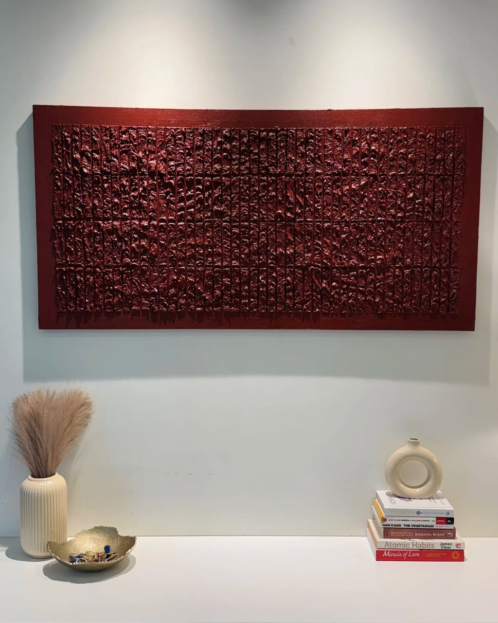 A rectangular red wooden wall art piece with intricate carved patterns, displayed on a white wall above a white console table in a modern room setting.