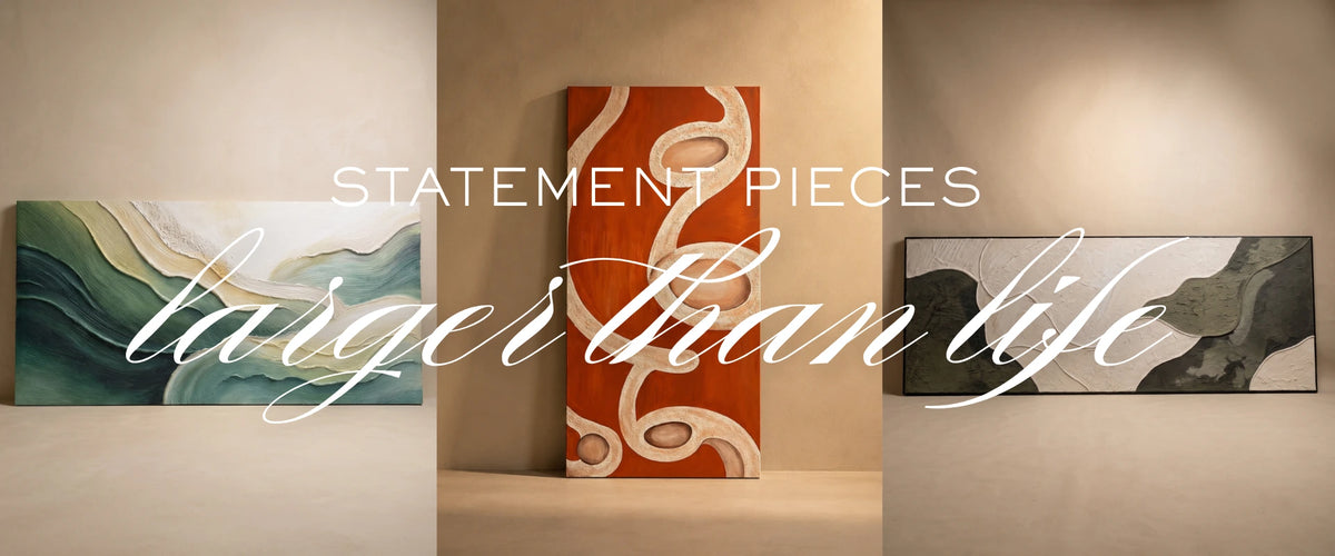 Three abstract canvas wall art pieces displayed side by side on beige walls, with large overlaid text reading 'STATEMENT PIECES larger than life'. The center canvas is orange with white flowing lines, while the side canvases feature green/blue waves and dark gray/black abstract forms.