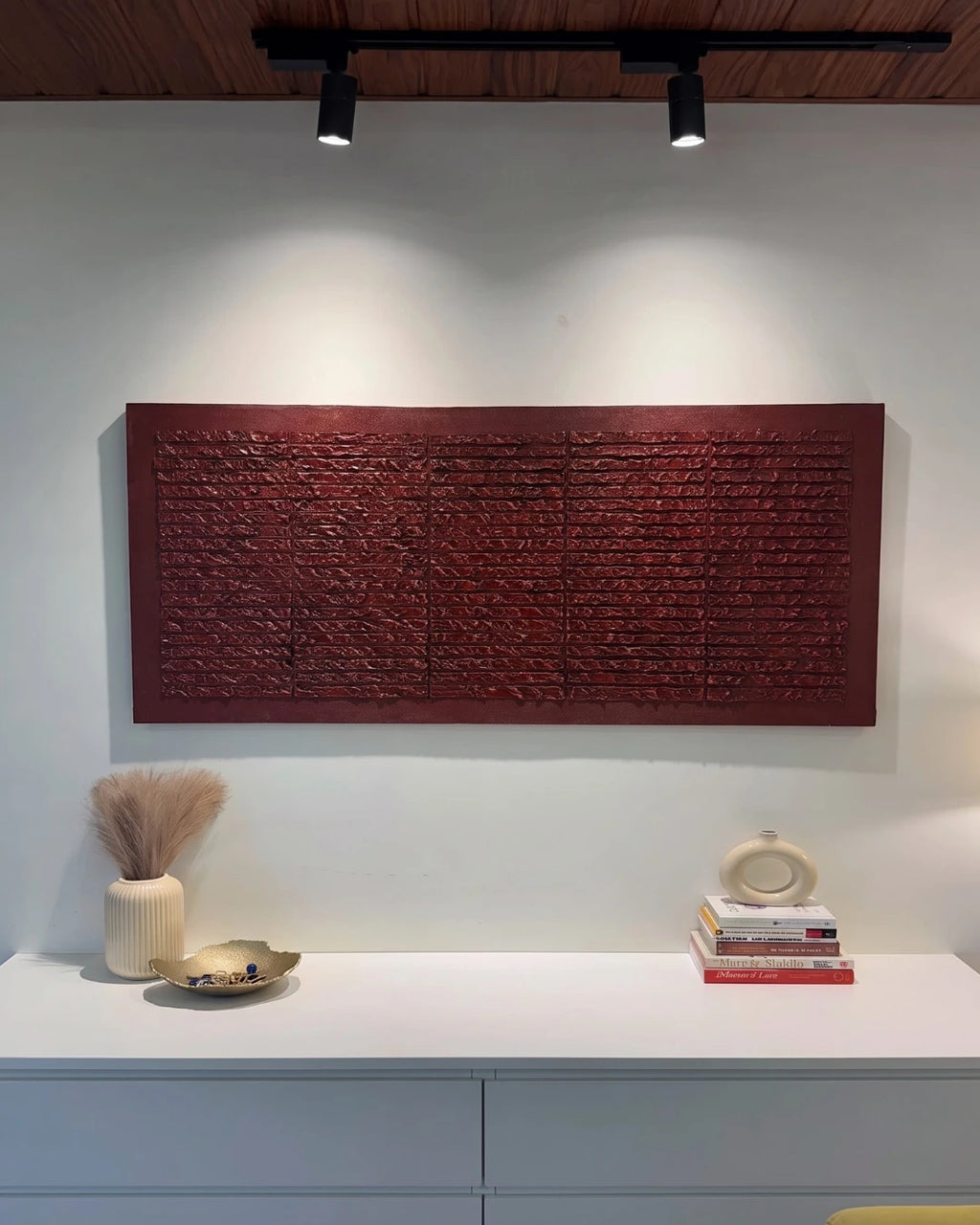 Brickwork deep red textured painting hanging above a console table with books and vases