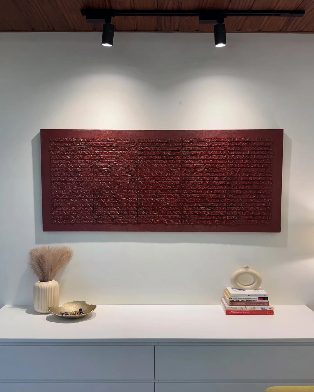 Brickwork deep red textured painting hanging above a console table with books and vases