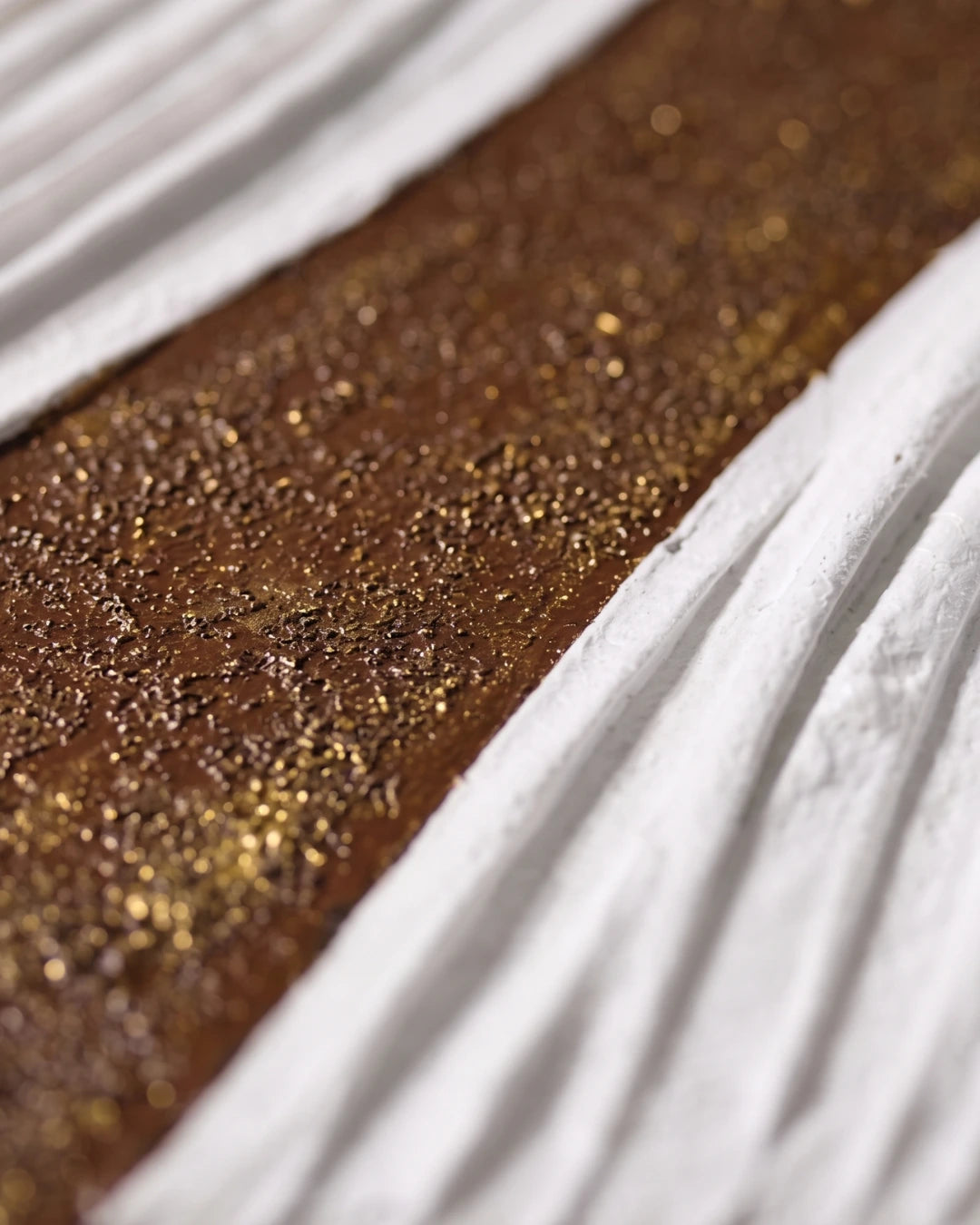 A close-up of a textured brown surface covered in fine gold glitter, bordered by white pleated fabric.
