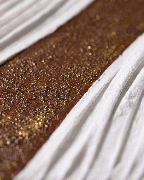 A close-up of a textured brown surface covered in fine gold glitter, bordered by white pleated fabric.