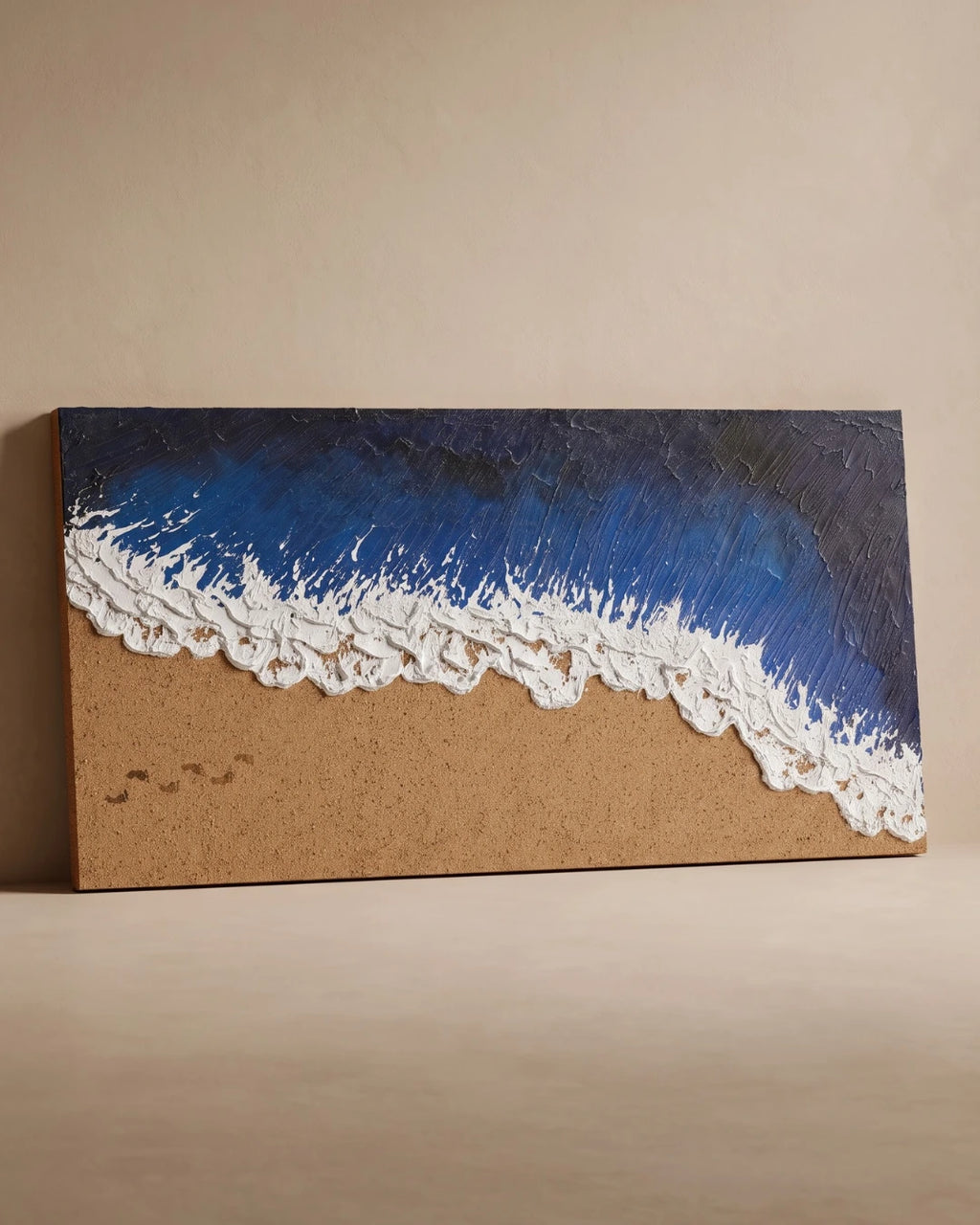 A rectangular canvas wall art piece depicting an ocean wave with textured blue and dark navy water, white foam, and a sandy beige shore, displayed against a plain beige wall.