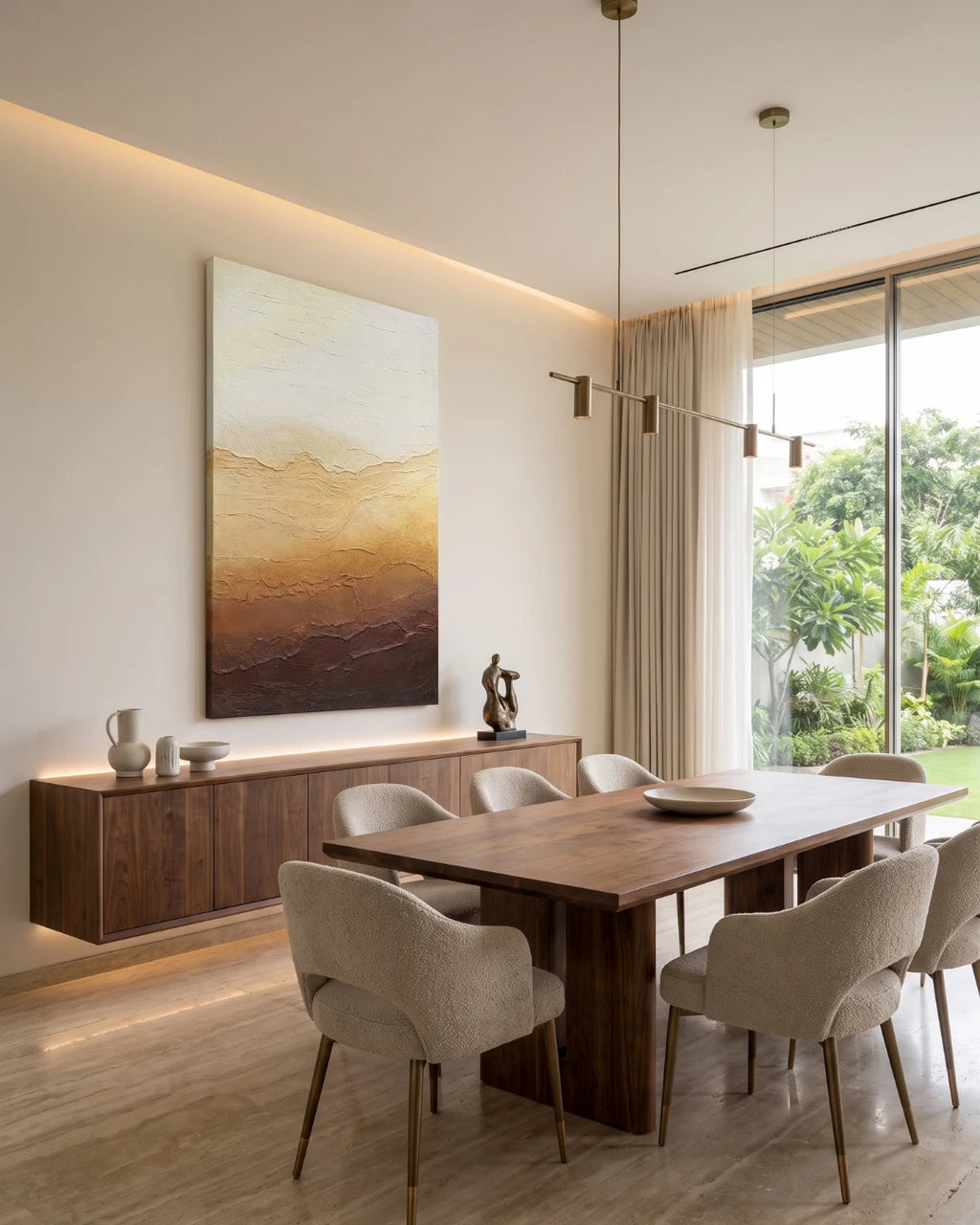 A modern dining room featuring a large vertical abstract landscape painting with golden and brown mountain-like layers, mounted above a dark wood sideboard. The dining table and six upholstered chairs are positioned in front of a large window looking out onto greenery.