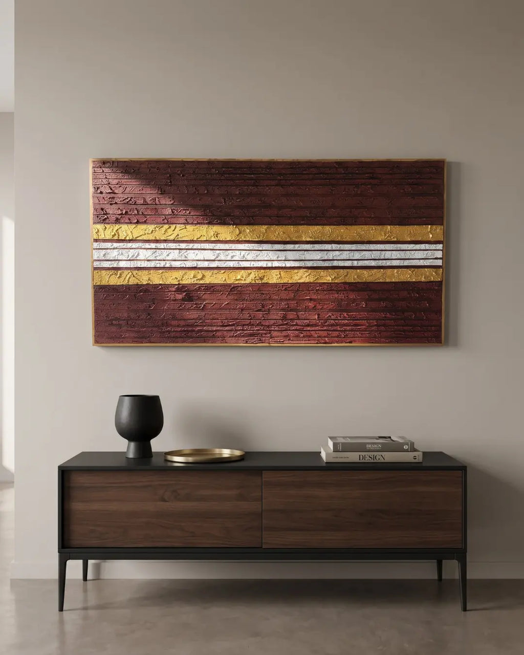 A modern living room setting featuring a large rectangular wall art piece with horizontal textured stripes in dark reddish-brown, metallic gold, and silver, hanging above a dark wood console table.