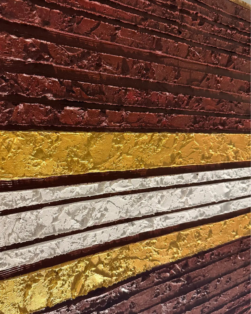 A close-up of a textured wall or panel with horizontal bands: dark reddish-brown at the top and bottom, a wide metallic gold band in the middle, and a white band running through the center.