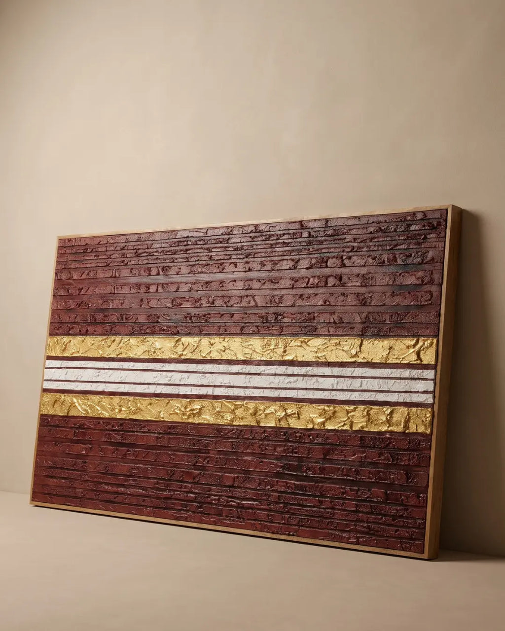 A framed textured wall art panel leaning against a beige wall on a matching floor. The artwork features horizontal bands of dark reddish-brown embossed texture, two metallic gold textured bands, and a central white textured band.