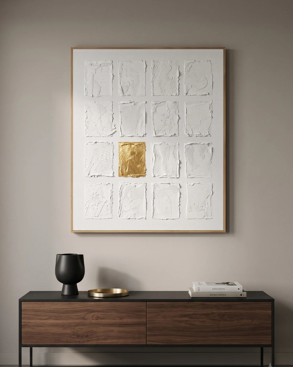 A framed abstract wall art piece hangs on a beige wall above a dark wood console table. The artwork features a white textured grid with a single metallic gold square in the center.